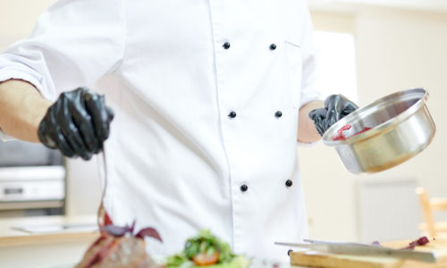 Portrait of handsome professional chef serving meat dish while cooking in modern restaurant kitchen